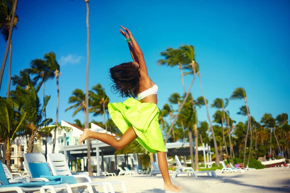 A woman joyfully leaps on a sunny palm-lined beach