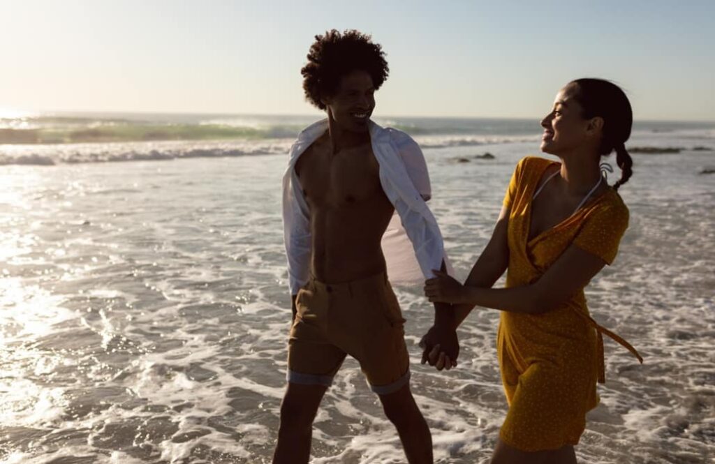 A joyful couple playfully walks along a sunny beach shore