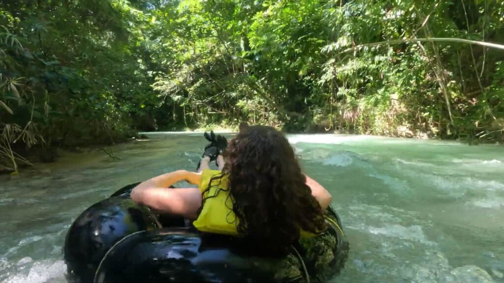 A person tubing down a serene, tree-lined river