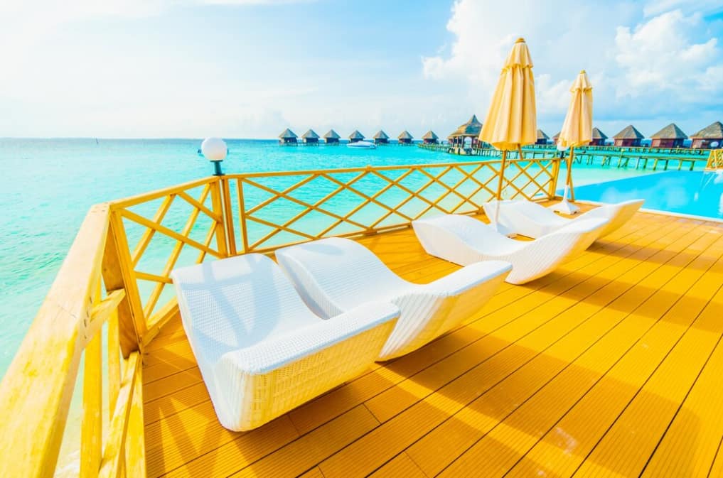 White loungers on a deck by turquoise waters and overwater villas