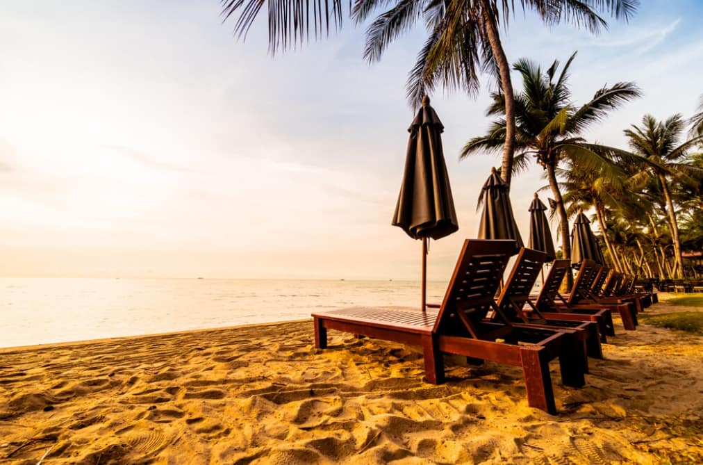 Wooden lounge chairs under umbrellas on a tropical beach at dusk
