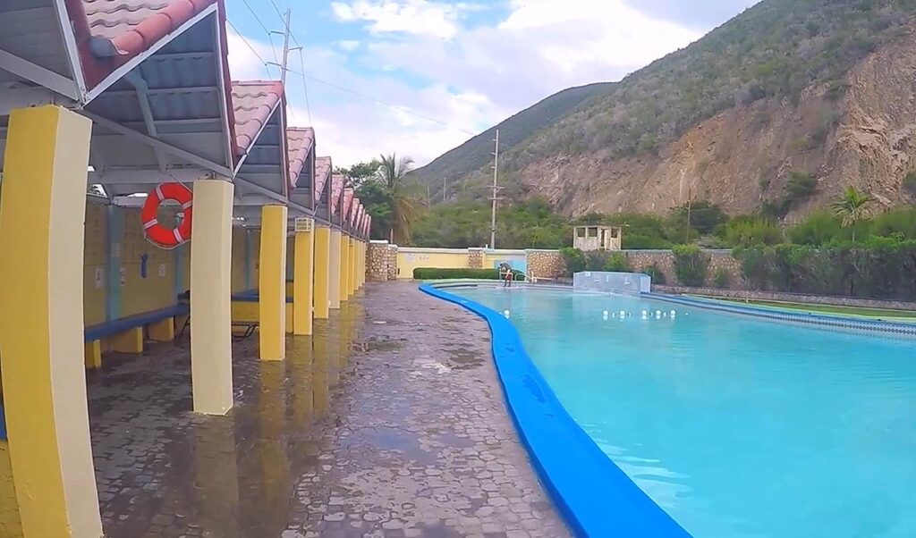 Empty poolside changing rooms partially flooded with water, under a cloudy sky
